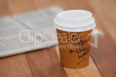 Close-up of disposable coffee cup and newspaper