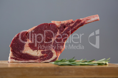 Rib chop steak and rosemary herb on wooden board against grey background