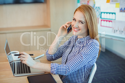 Female graphic designer talking on mobile phone while working in office