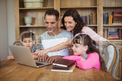 Parents and kids using laptop on table in study room