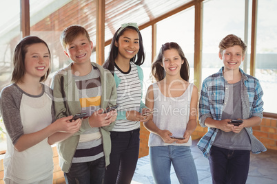 Portrait of smiling school friends using mobile phone in corridor