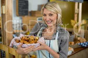 Portrait of smiling female staff holding a basket of baked snacks at counter