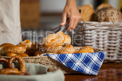 Staff holding bread with tong in bakery shop