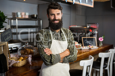 Portrait of smiling male staff standing with arms crossed at counter
