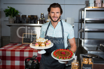 Portrait of male staff holding dessert on cake stand at counter