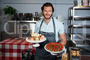 Portrait of male staff holding dessert on cake stand at counter