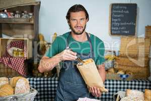 Portrait of male staff packing bread in paper bag
