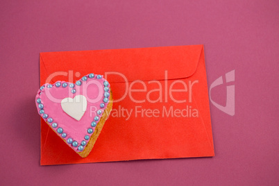 Heart shape cookie on red envelope against pink background