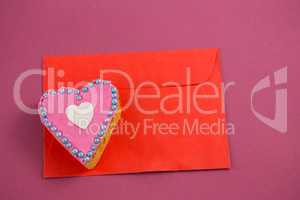 Heart shape cookie on red envelope against pink background