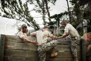 Soldiers helping man to climb wooden wall