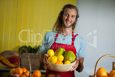 Smiling male staff holding fruits in basket at organic section