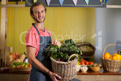 Smiling male staff holding leafy vegetables in basket at organic section