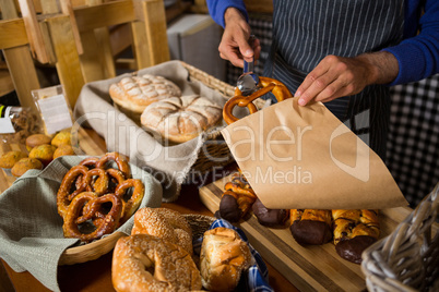 Mid section of staff packing croissant in paper bag at counter