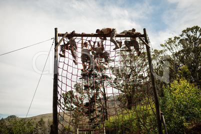 Military soldiers climbing rope during obstacle course