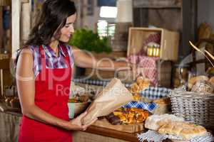 Smiling female staff packing sweet food in paper bag at counter