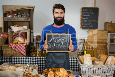 Portrait of smiling male staff holding board with open sign at counter