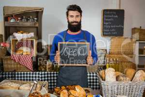 Portrait of smiling male staff holding board with open sign at counter