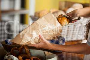 Staff packing bread in paper bag at bakery shop