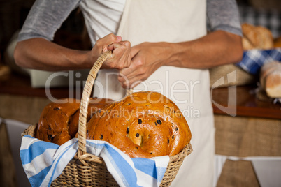 Mid-section of female staff holding wicker basket of breads at counter