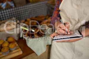 Mid section of female staff writing on notepad at bread counter