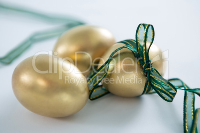 Golden Easter eggs tied with ribbon on white background