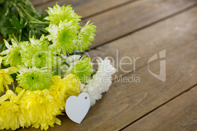 Bunch of yellow flowers with heart shape tag on wooden plank
