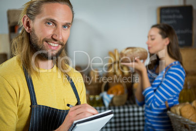 Smiling male staff writing on notepad at counter