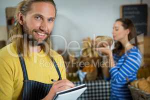 Smiling male staff writing on notepad at counter