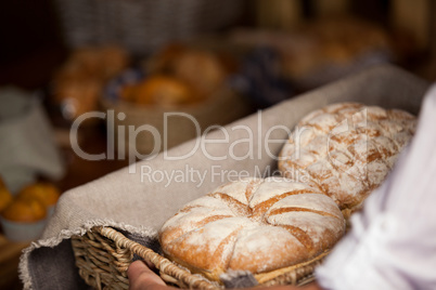 Hand of female staff holding basket of sweet foods in bakery section