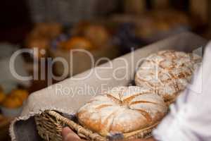 Hand of female staff holding basket of sweet foods in bakery section