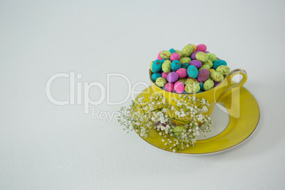 Cup filled with colorful chocolate Easter eggs and white flower