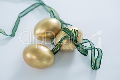 Golden Easter eggs tied with ribbon on white background