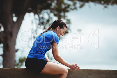 Fit woman sitting over wooden wall obstacle