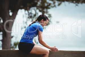 Fit woman sitting over wooden wall obstacle