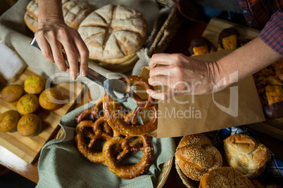 Mid section of staff packing pretzel bread in paper bag at counter