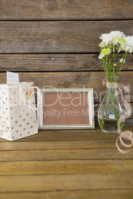 Gift bag, photo frame and flower vase on wooden surface