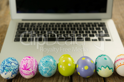 Painted Easter eggs and laptop on wooden surface