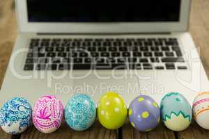 Painted Easter eggs and laptop on wooden surface