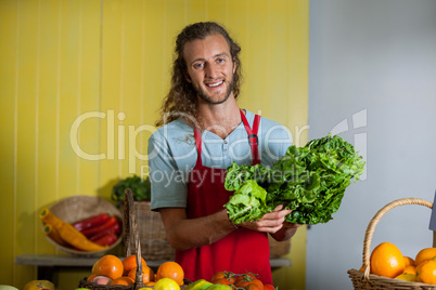 Smiling staff holding leafy vegetables at counter in market