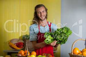 Smiling staff holding leafy vegetables at counter in market