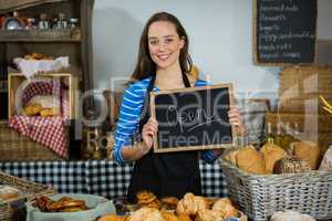 Portrait of smiling female staff holding chalkboard with open sign at counter