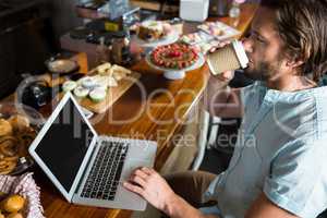Man having coffee while using laptop at counter
