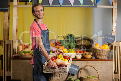 Smiling male staff holding fresh vegetables in basket at organic section