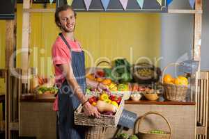 Smiling male staff holding fresh vegetables in basket at organic section
