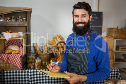 Smiling male staff writing on clipboard at counter in bakery shop