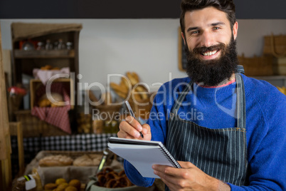 Smiling male staff writing on notepad at counter in bakery shop