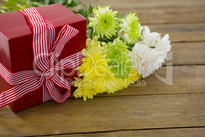 Gift box and bunch of yellow flowers on wooden plank