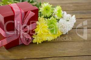 Gift box and bunch of yellow flowers on wooden plank