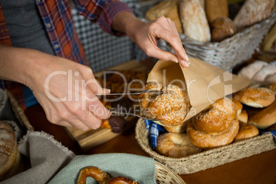 Mid section of staff packing croissant in paper bag at counter