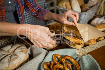 Mid section of staff packing pretzel bread in paper bag at counter